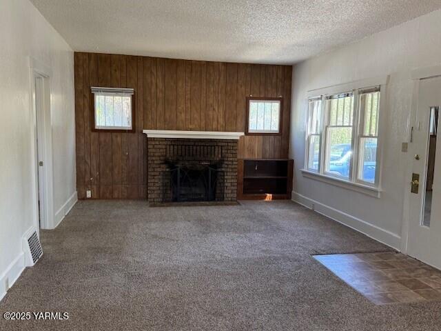1216 S 44th Ave, Yakima, WA 98908 - unfurnished living room featuring carpet flooring, a fireplace, a textured ceiling, wooden walls, and baseboards
