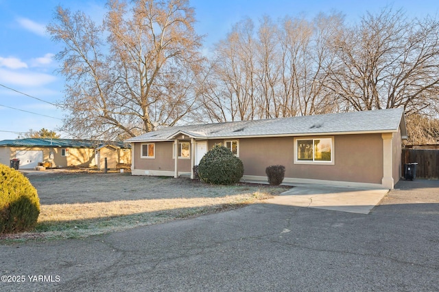 single story home with a shingled roof, a front lawn, and stucco siding