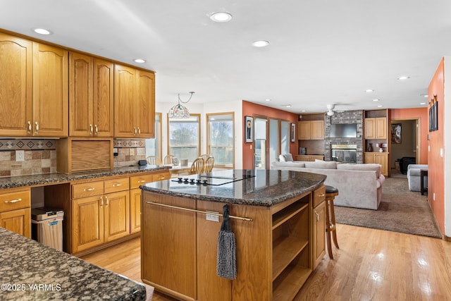 kitchen featuring open floor plan, dark stone countertops, a center island, light wood-type flooring, and a brick fireplace