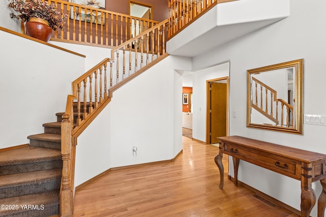 stairway featuring a high ceiling, baseboards, and wood finished floors