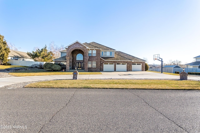 view of front facade with a front yard, concrete driveway, brick siding, and fence