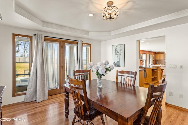 dining space with light wood-style floors, a tray ceiling, baseboards, and an inviting chandelier