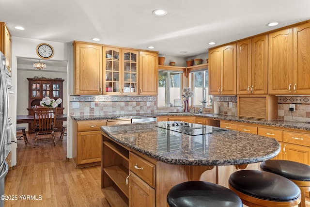 kitchen featuring a center island, black electric stovetop, glass insert cabinets, a sink, and dark stone countertops