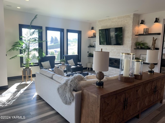 living room with a stone fireplace, dark wood-type flooring, and baseboards