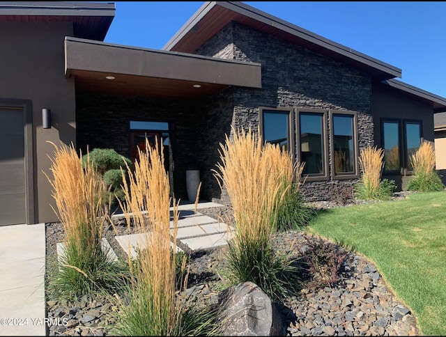 rear view of property featuring a yard, stone siding, and stucco siding