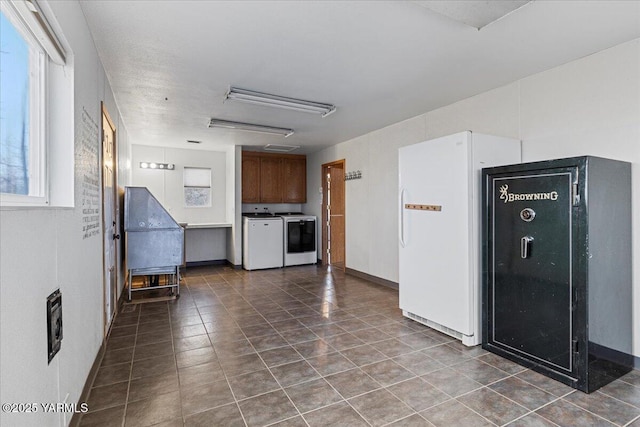 kitchen with dark tile patterned flooring, brown cabinetry, washer and clothes dryer, and freestanding refrigerator