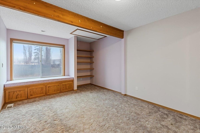 unfurnished room featuring attic access, light colored carpet, beamed ceiling, and a textured ceiling