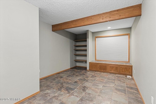 unfurnished room featuring stone finish flooring, beamed ceiling, a textured ceiling, and baseboards