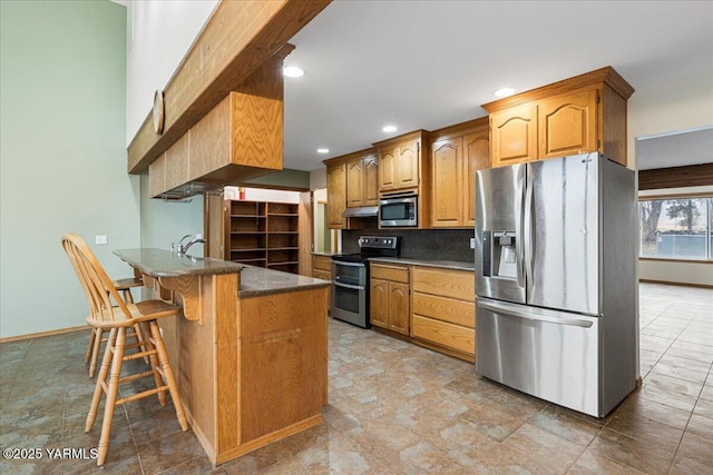 kitchen featuring a breakfast bar, brown cabinets, dark countertops, appliances with stainless steel finishes, and a peninsula