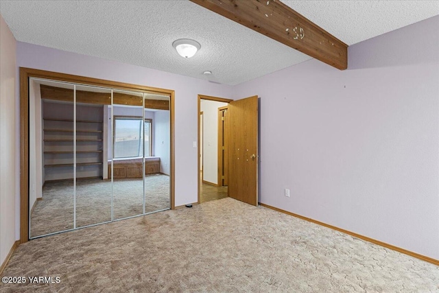 unfurnished bedroom with baseboards, carpet, beam ceiling, a textured ceiling, and a closet