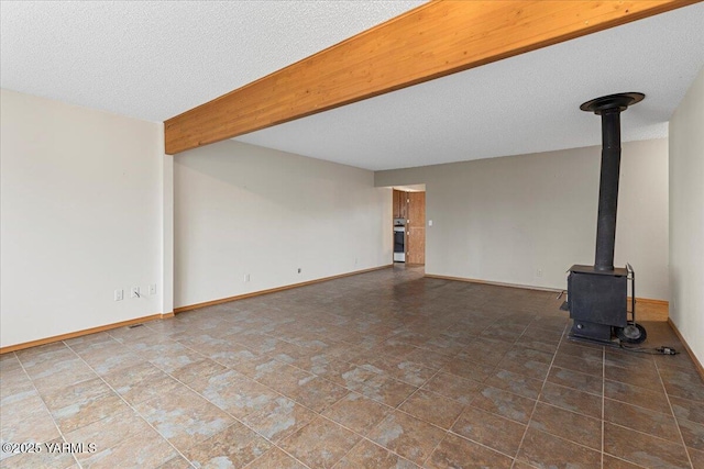 unfurnished living room featuring a wood stove, a textured ceiling, baseboards, and beam ceiling