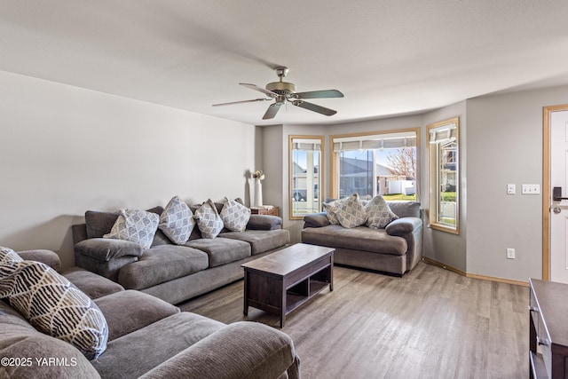 living area with baseboards, a ceiling fan, and light wood finished floors
