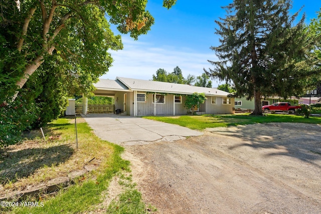 ranch-style home with dirt driveway, an attached carport, and a front yard