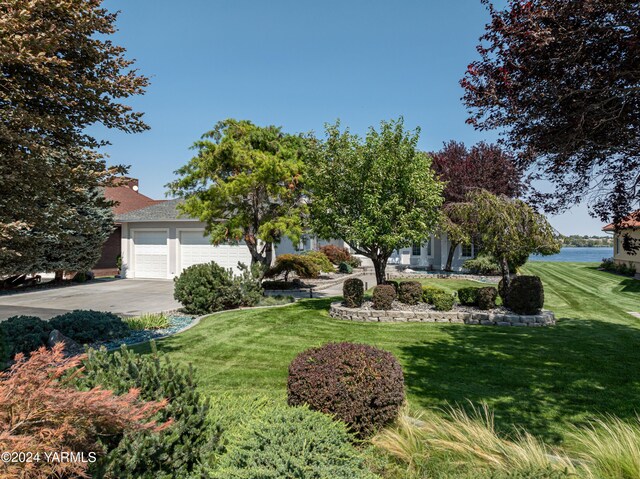 view of property hidden behind natural elements with a garage, a front yard, a water view, and driveway