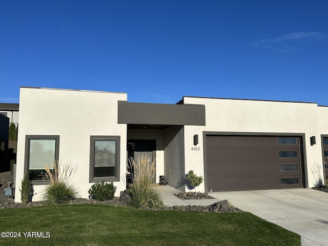 modern home with a garage, driveway, a front lawn, and stucco siding