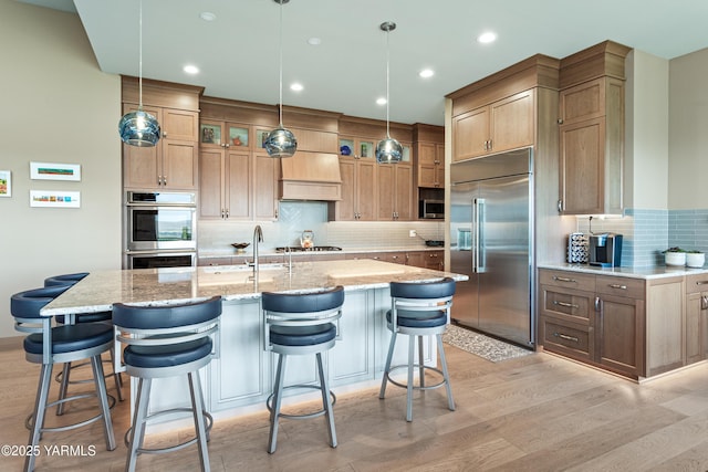 5506 Marilane St, Yakima, WA 98908 - kitchen featuring appliances with stainless steel finishes, backsplash, light stone counters, light wood-type flooring, and glass insert cabinets