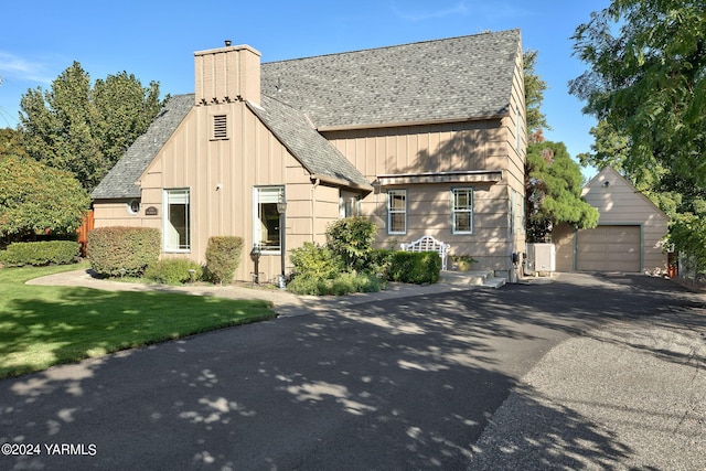 view of front of house featuring an outbuilding, a detached garage, a chimney, a shingled roof, and driveway