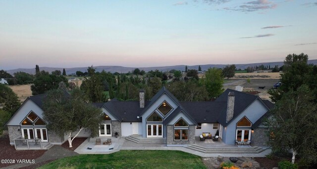 back of house featuring a yard, french doors, stone siding, a chimney, and a patio area