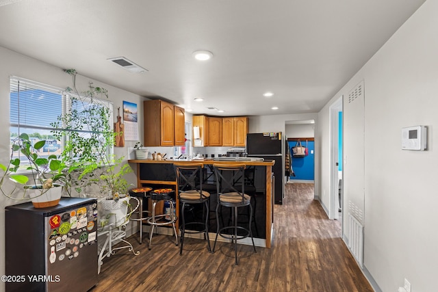 kitchen with freestanding refrigerator, dark wood-style flooring, recessed lighting, a peninsula, and brown cabinetry