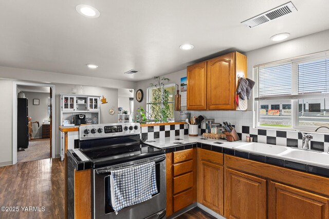 kitchen with stainless steel electric range, a peninsula, dark wood-type flooring, brown cabinets, and recessed lighting