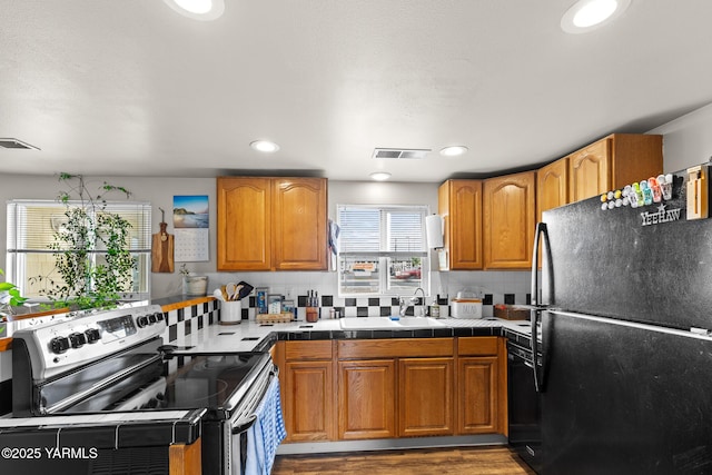 kitchen featuring black appliances, a sink, backsplash, brown cabinetry, and recessed lighting