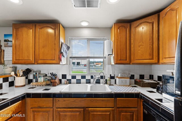 kitchen featuring backsplash, tile counters, black dishwasher, a sink, and brown cabinets