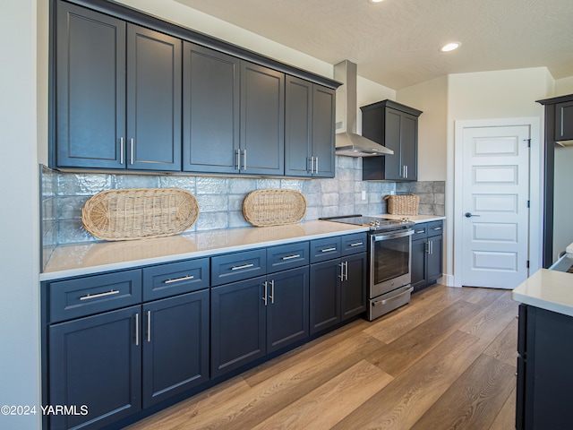 kitchen featuring tasteful backsplash, electric range, wood finished floors, light countertops, and wall chimney range hood