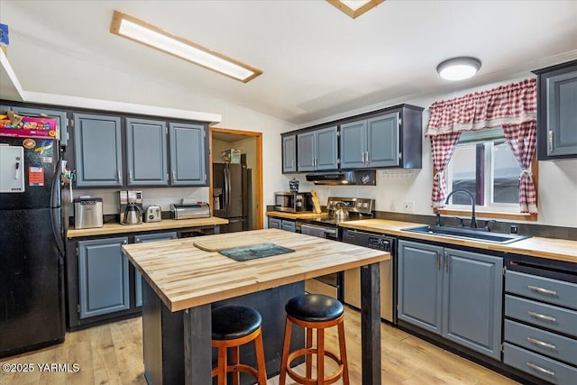 kitchen featuring stainless steel appliances, a sink, wood counters, and blue cabinetry