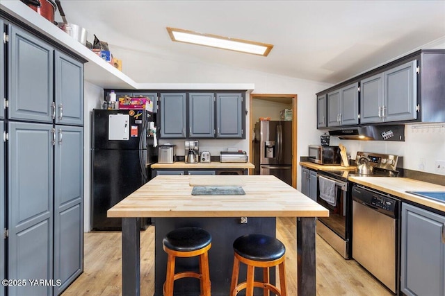 kitchen featuring vaulted ceiling, appliances with stainless steel finishes, light wood finished floors, and under cabinet range hood