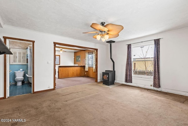 unfurnished living room featuring a wood stove, ceiling fan, carpet floors, and a textured ceiling