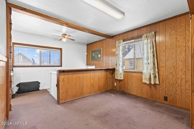 interior space featuring carpet floors, wood walls, a ceiling fan, and beam ceiling