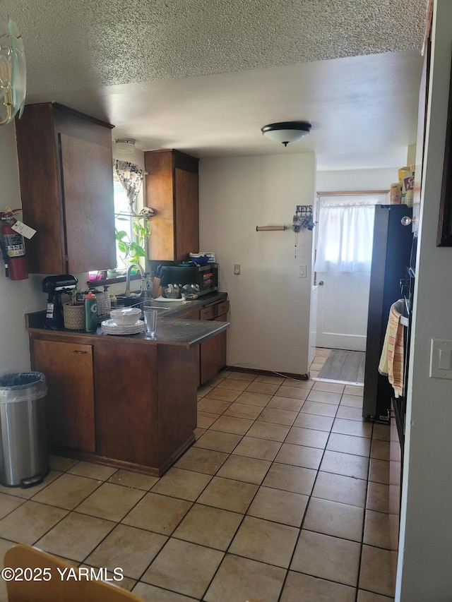 kitchen featuring a textured ceiling, light tile patterned floors, a sink, dark countertops, and a peninsula