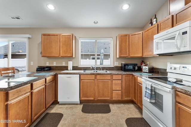 kitchen featuring visible vents, a sink, white appliances, a peninsula, and a healthy amount of sunlight