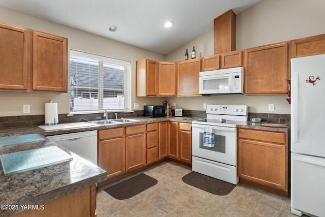 kitchen with white appliances, dark countertops, lofted ceiling, and a sink