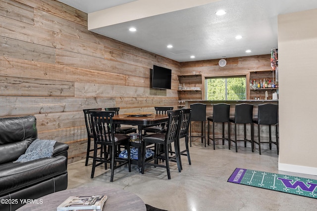 dining room featuring recessed lighting, wood walls, finished concrete flooring, and a dry bar