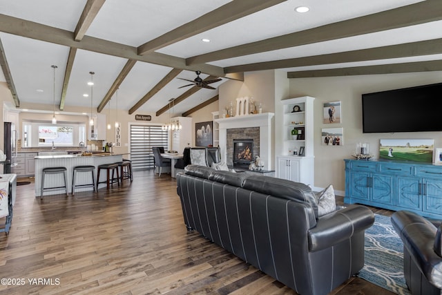 living area featuring a fireplace, wood finished floors, lofted ceiling with beams, ceiling fan with notable chandelier, and recessed lighting