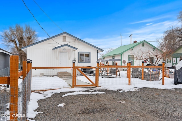 snow covered rear of property featuring a fenced front yard and a gate