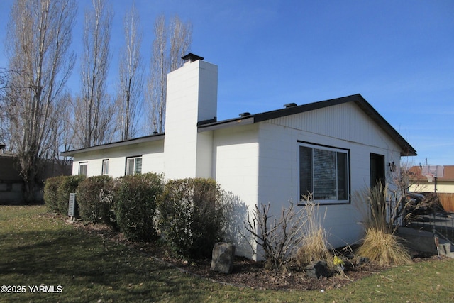 view of side of home featuring a lawn, concrete block siding, and a chimney