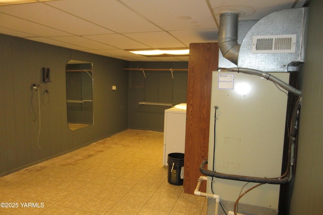 basement featuring wooden walls, heating unit, washer / dryer, a drop ceiling, and tile patterned floors