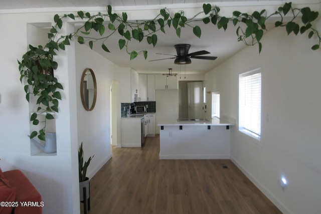 kitchen with wood finished floors, a peninsula, white cabinets, light countertops, and decorative backsplash