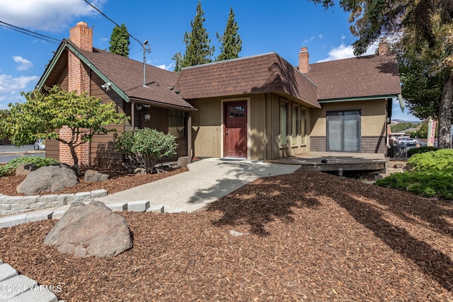 view of front of home featuring a shingled roof, a chimney, brick siding, and mansard roof