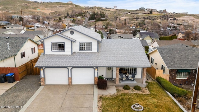 traditional home featuring fence, a residential view, concrete driveway, a shingled roof, and a garage