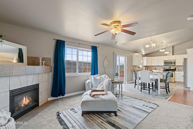 living area featuring light tile patterned floors, baseboards, lofted ceiling, a tile fireplace, and ceiling fan with notable chandelier