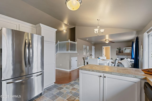 kitchen featuring tile countertops, lofted ceiling, freestanding refrigerator, white cabinets, and ceiling fan with notable chandelier