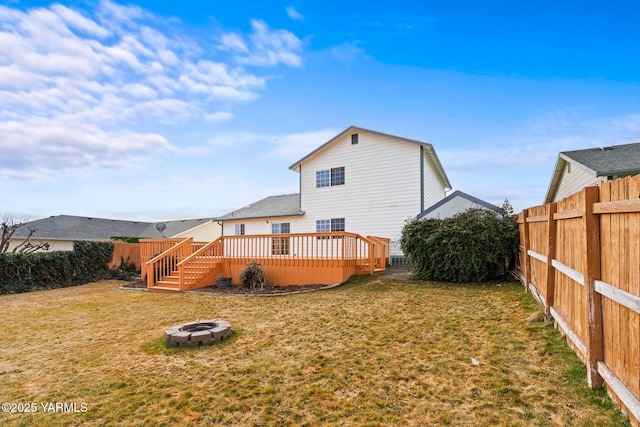 back of property with a deck, a fenced backyard, a lawn, and an outdoor fire pit