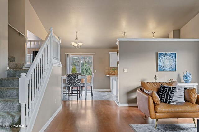 living room featuring stairs, baseboards, light wood finished floors, and a chandelier