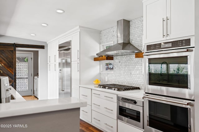 5709 Marilane St, Yakima, WA 98908 - kitchen with wall chimney range hood, appliances with stainless steel finishes, white cabinetry, backsplash, and a barn door