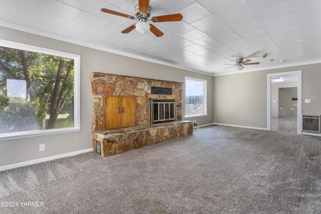 unfurnished living room featuring baseboards, heating unit, crown molding, a stone fireplace, and carpet floors