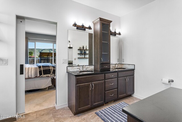 full bathroom with ensuite bathroom, double vanity, a sink, and baseboards