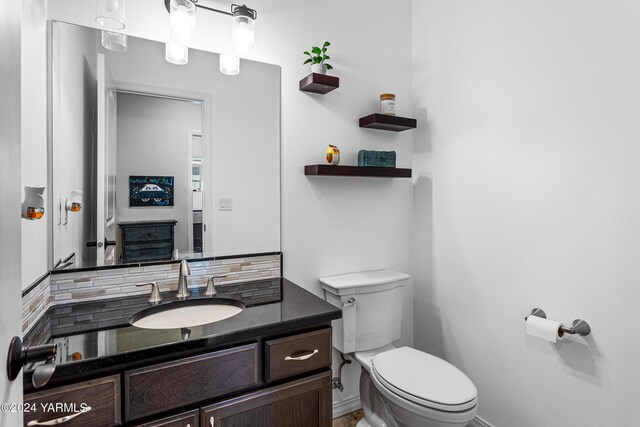 half bath featuring toilet, baseboards, decorative backsplash, and vanity